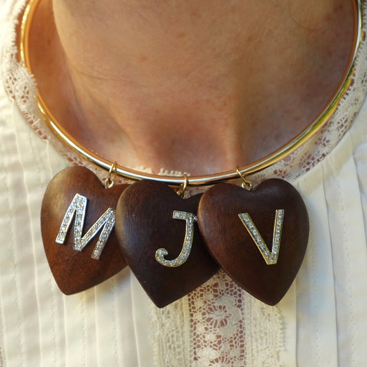 Necklace with heart-shaped pendants with 'MJV' diamond letters on a person wearing a lace shirt