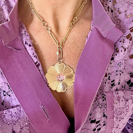 Gold necklace with a floral pendant on a person wearing a purple lace garment.
