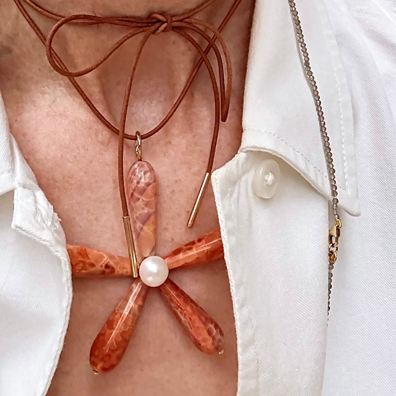 Necklace with a unique design featuring a pearl and brown cord on a white shirt background