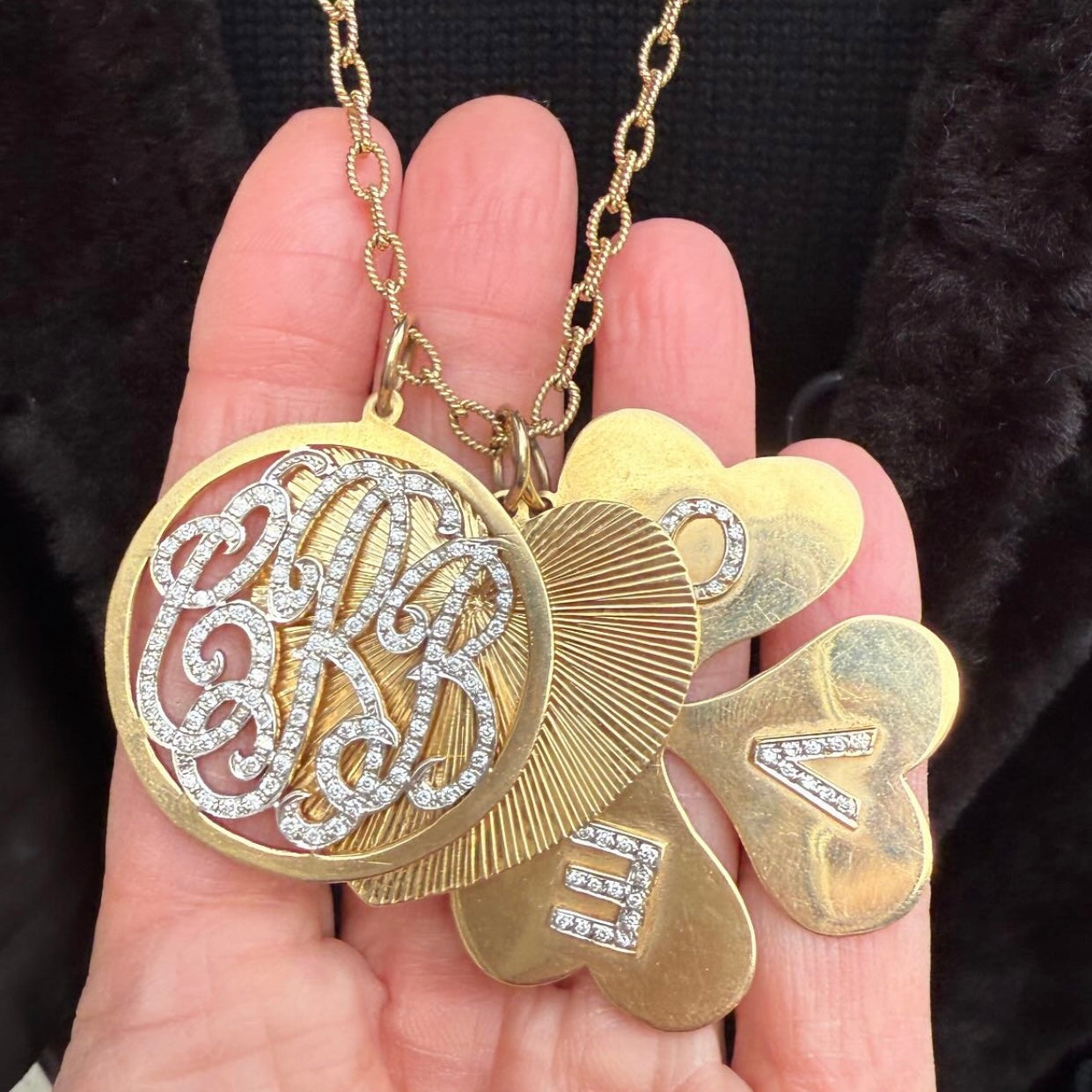 Gold necklace with multiple layered pendants held in a hand against a dark background