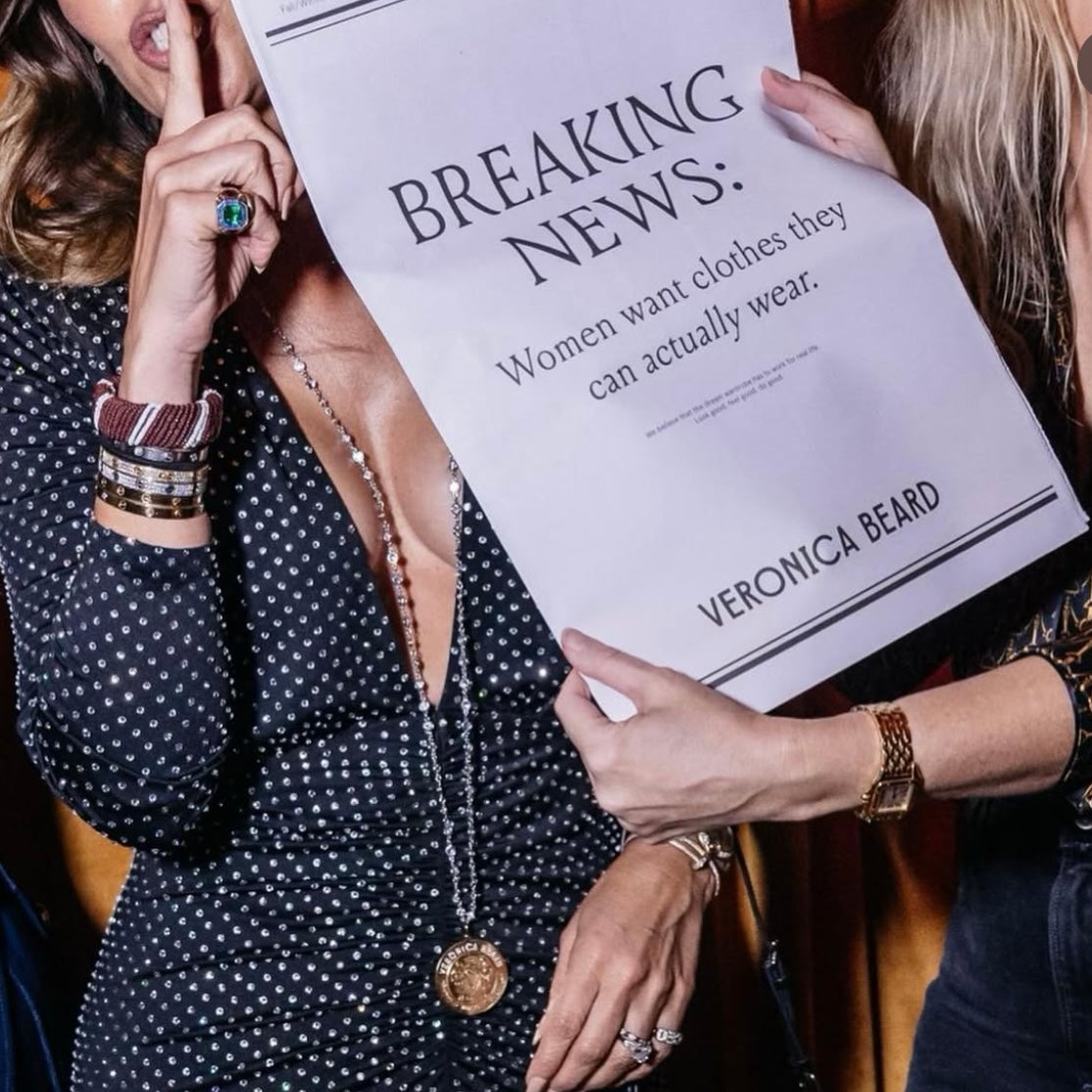 Person holding a sign with 'VERONICA BEARD' and 'BREAKING NEWS: Women want clothes theycan actually wear.'