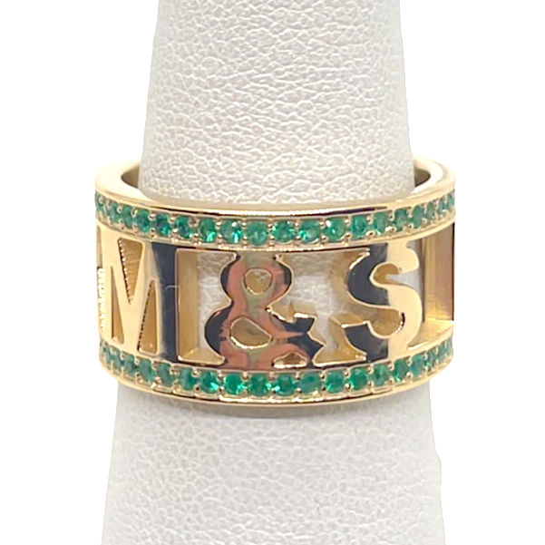 A 14k yellow gold ring with pave emeralds, displayed on a clear gemstone holder.