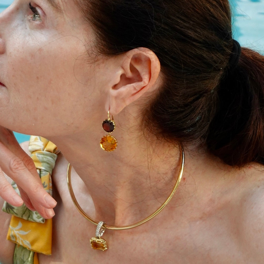 Close-up of a woman wearing gold hoop earrings with gemstones.
