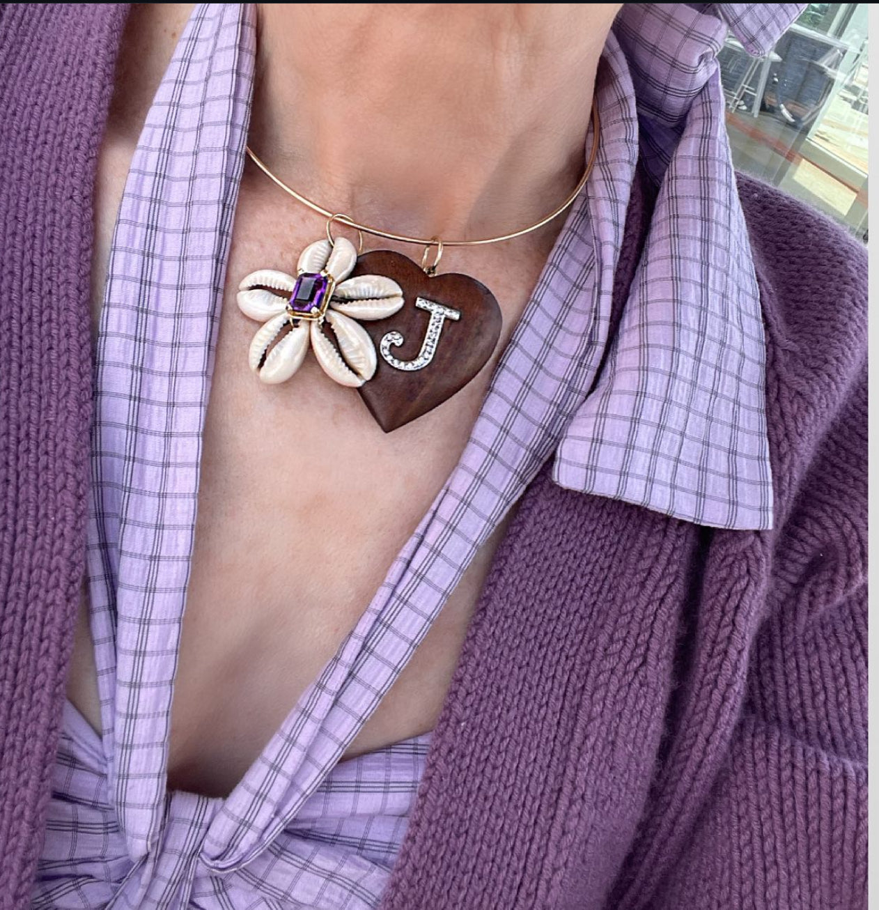 Necklace with a heart pendant featuring a letter 'J' and floral design, worn by a person in a purple cardigan.