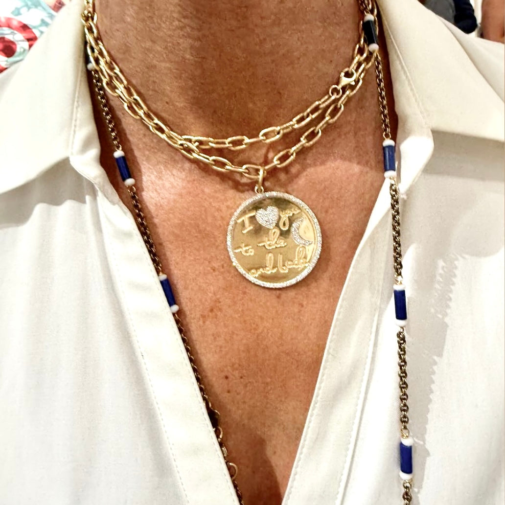 Close-up of a person wearing a gold necklace with a pendant, white shirt, and colorful background.