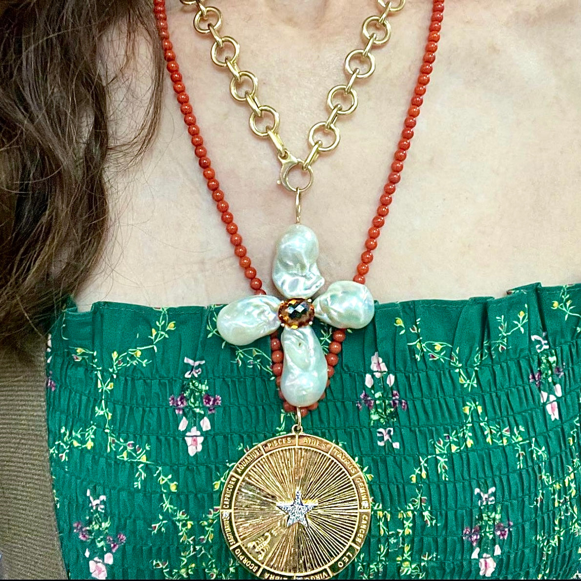 Necklace with floral pendant and gold medallion worn by a person in a green floral top.
