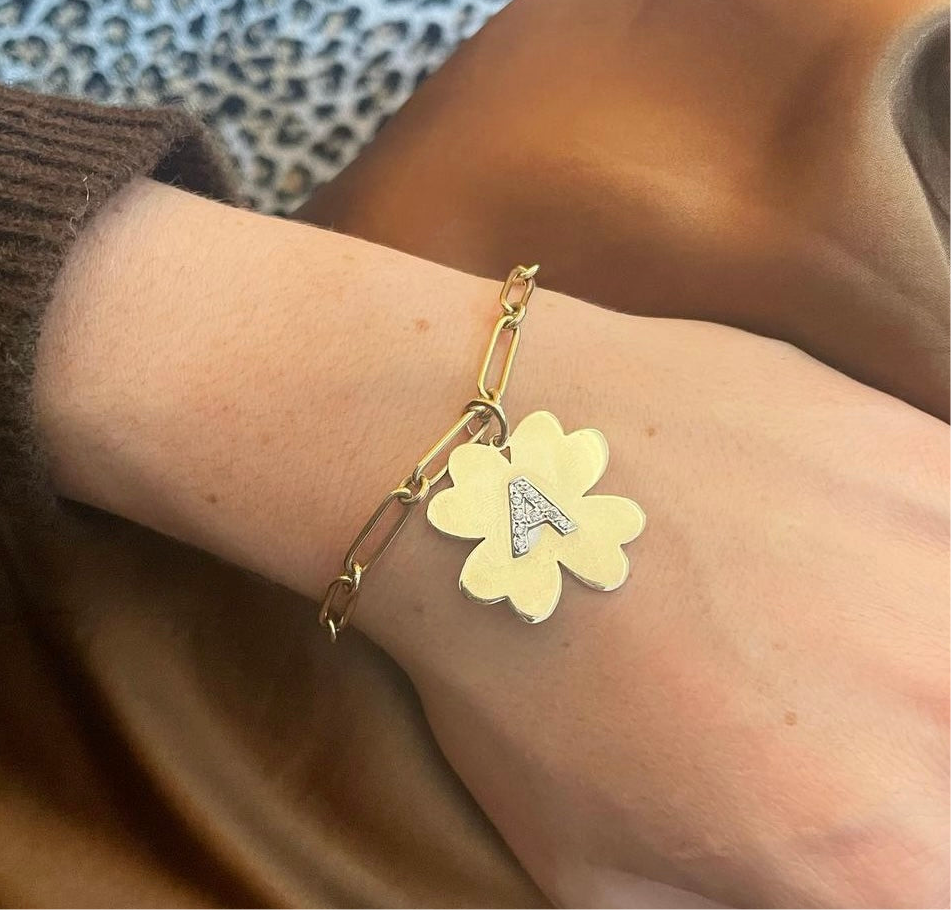 Gold bracelet with a yellow clover charm and letter 'A' on a wrist.