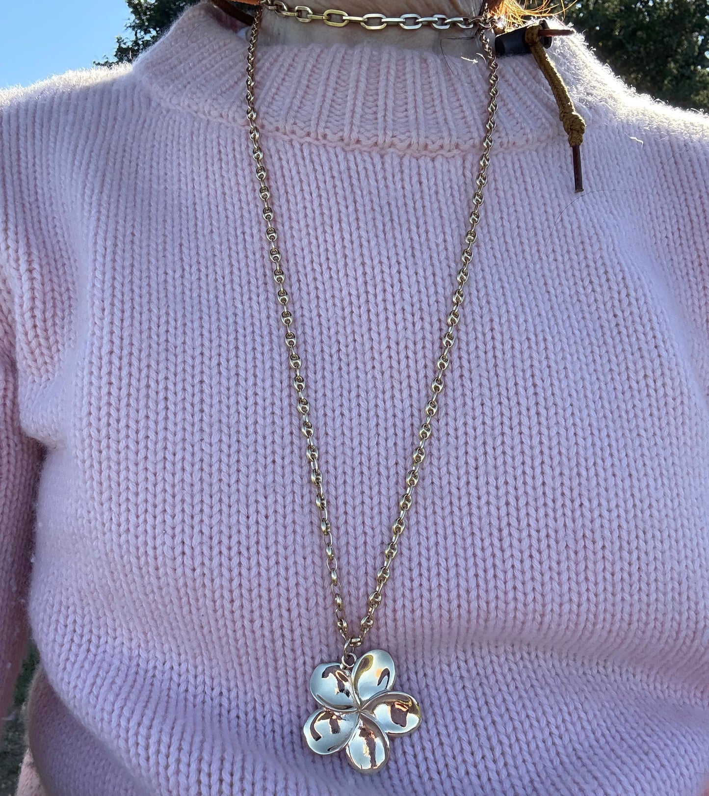 Necklace with a flower pendant on a light purple shirt against a blurred natural background