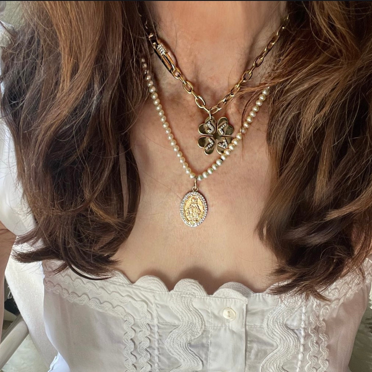 Close-up of a person wearing a gold necklace with a clover pendant and a pearl strand.