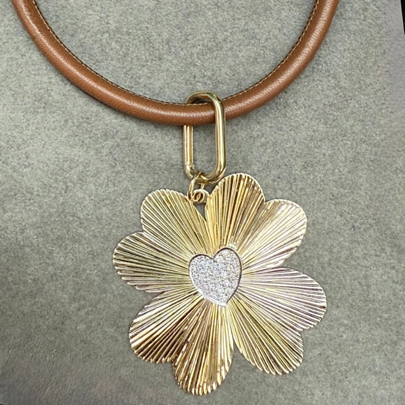Gold clover-shaped pendant with a heart in the center on a brown leather strap.