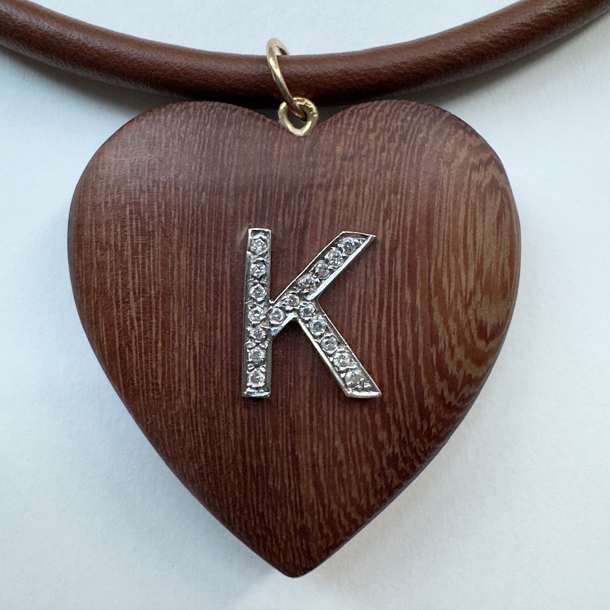 Heart-shaped wooden pendant with a silver 'K' charm on a white background