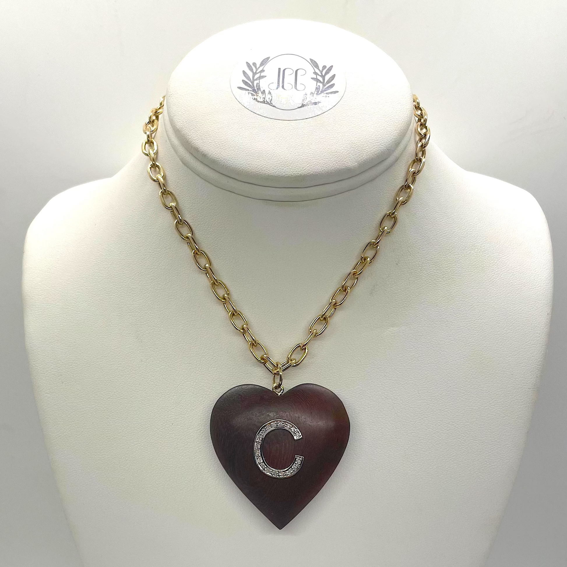 Necklace with a heart-shaped wooden pendant on a mannequin bust with the letter C in diamonds. 