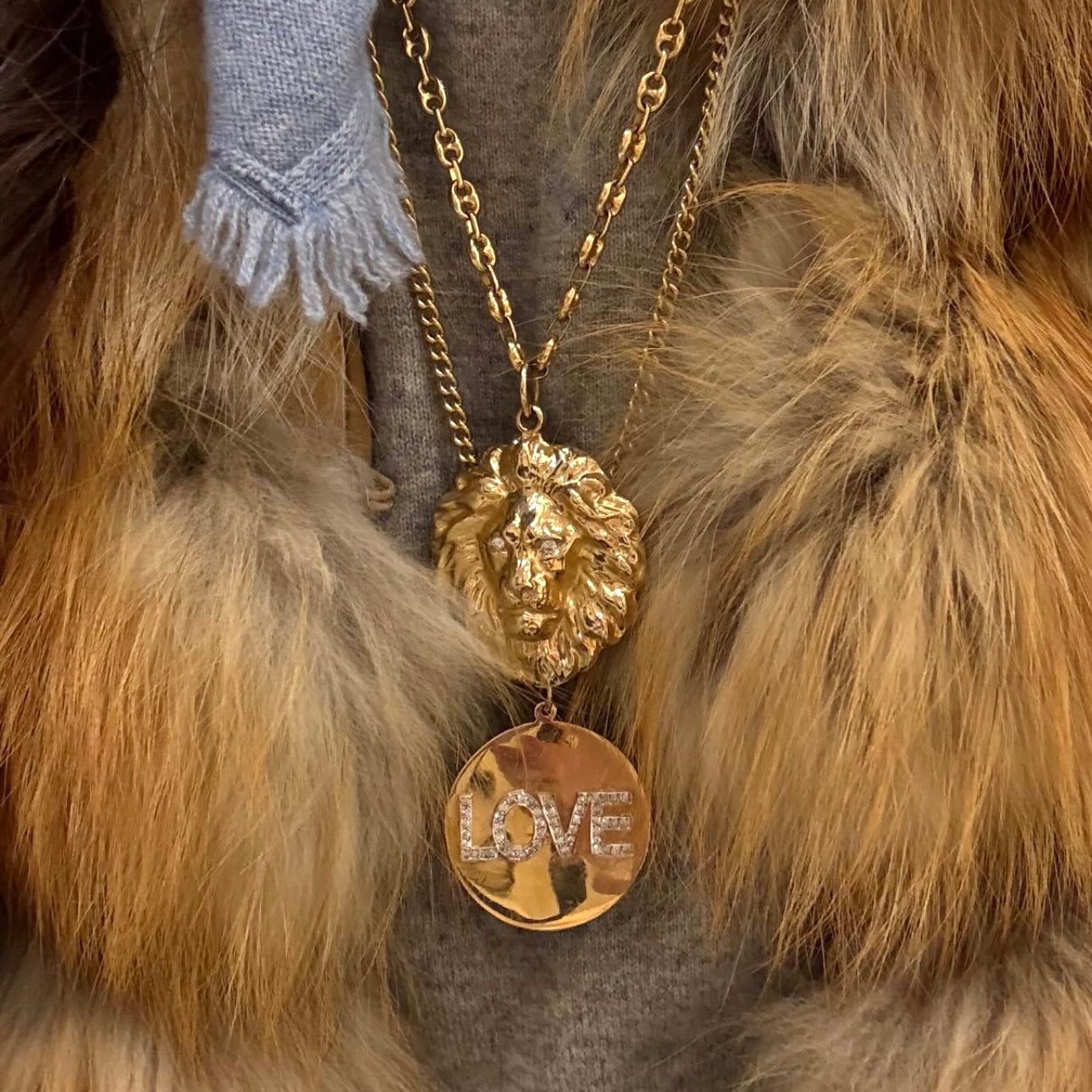 Gold necklace with lion head pendant and 'LOVE' charm on fur background