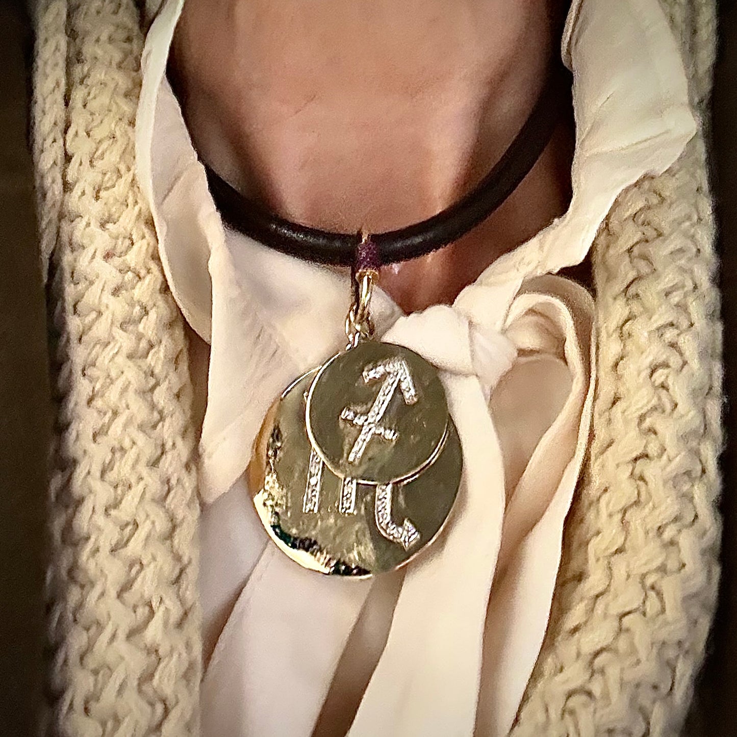 Necklace with two layered round pendants featuring Sagittarius and Scorpio symbols worn by a person in a white shirt and beige scarf.