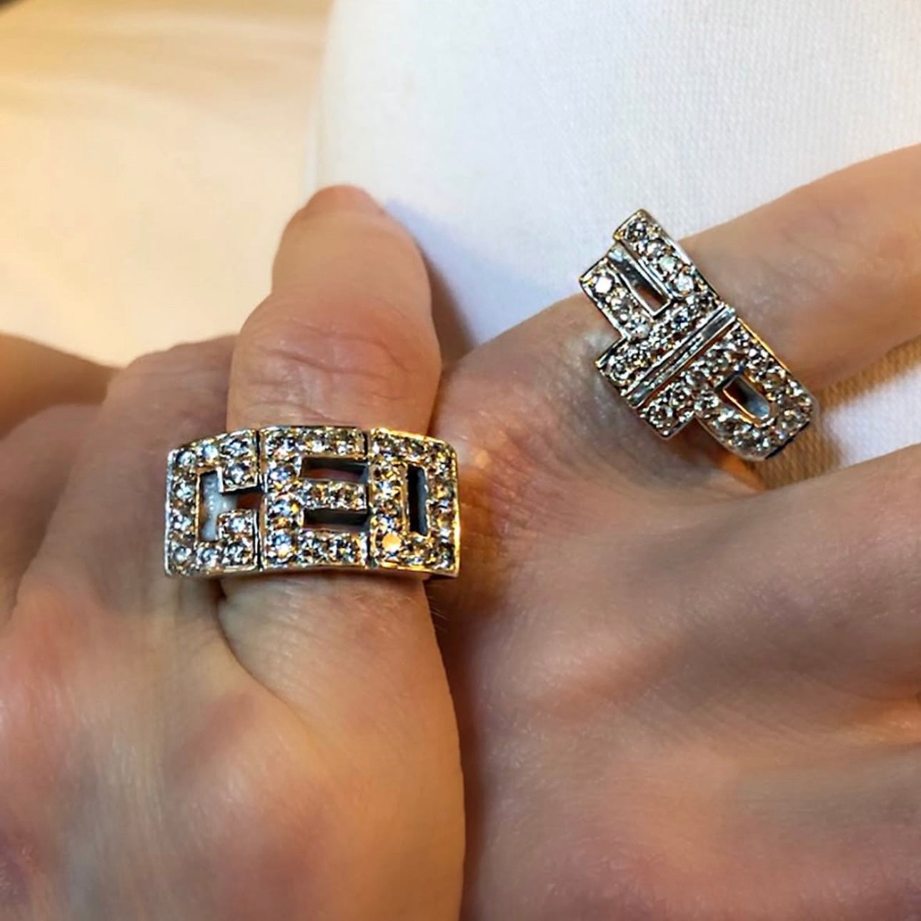 Two diamond-encrusted rings on a person's fingers with a neutral background
