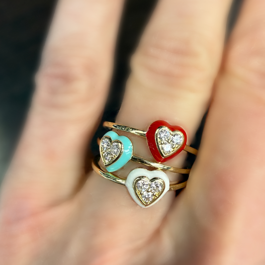 Three heart-shaped gold rings in red, blue, and white on a finger with a blurred background