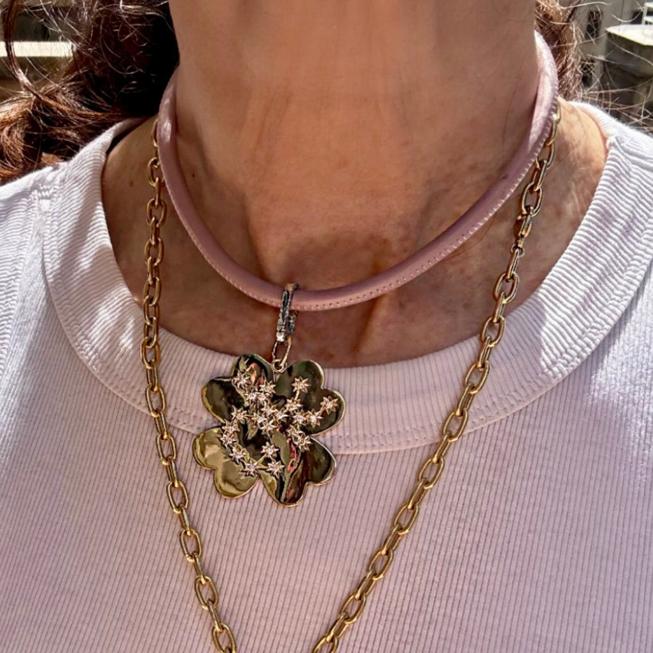 Close-up of a person wearing a gold chain necklace with a clover-shaped pendant.