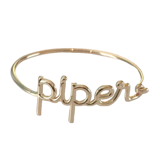 A 14k yellow gold wire script name bracelet with the name 'piper' written out on a white background