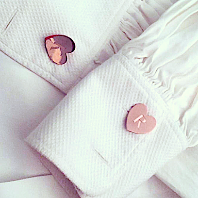 A white shirt with a pair of rose gold cufflinks that have the letter 'R' engraved on them.
