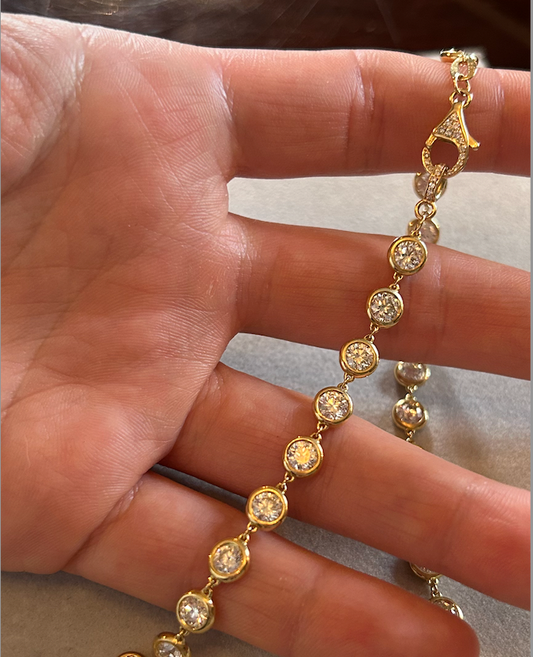 A hand holding a yellow gold diamond chain necklace with multiple round diamond pendants.