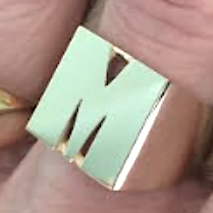 A 14k yellow gold initial ring on a person's finger, the ring has a shiny finish and is adorned with a single letter 'M'.