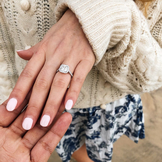 Close-up of two hands with a diamond ring, wearing a beige sweater and floral dress.