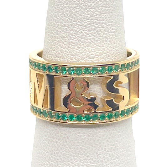A 14k yellow gold ring with pave emeralds, displayed on a clear gemstone holder.
